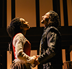 With the shadowed black outline of the wood superstructure behind them, Agnes in Simple Elizabethan dress and William in Elizabehtn leather jacket hold hands. He's looking up to the heavens, she's looking up toward his eyes.